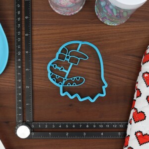 May include: A blue plastic cookie cutter shaped like a cartoon ghost with a toothy grin and a single eye.