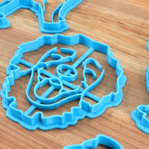 May include: A set of blue plastic cookie cutters in various shapes, including a flower, a heart, and a star. The cutters are on a wooden surface.