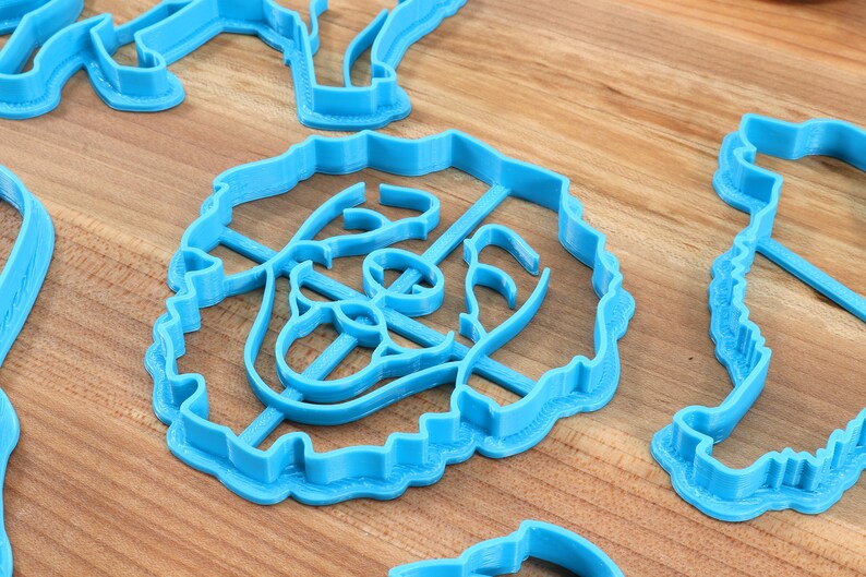 May include: A set of blue plastic cookie cutters in various shapes, including a flower, a heart, and a star. The cutters are on a wooden surface.