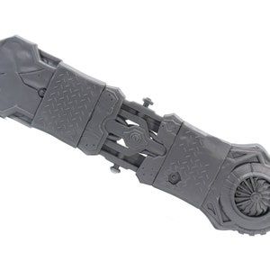 May include: A gray plastic toy weapon with a detailed design, featuring a rotating blade and a textured surface.