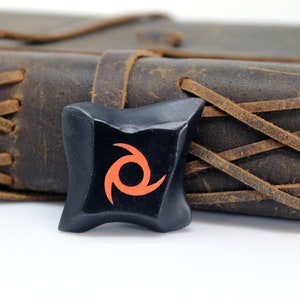 May include: A black leather-bound journal with brown leather straps and a black and orange swirl design on the front cover.
