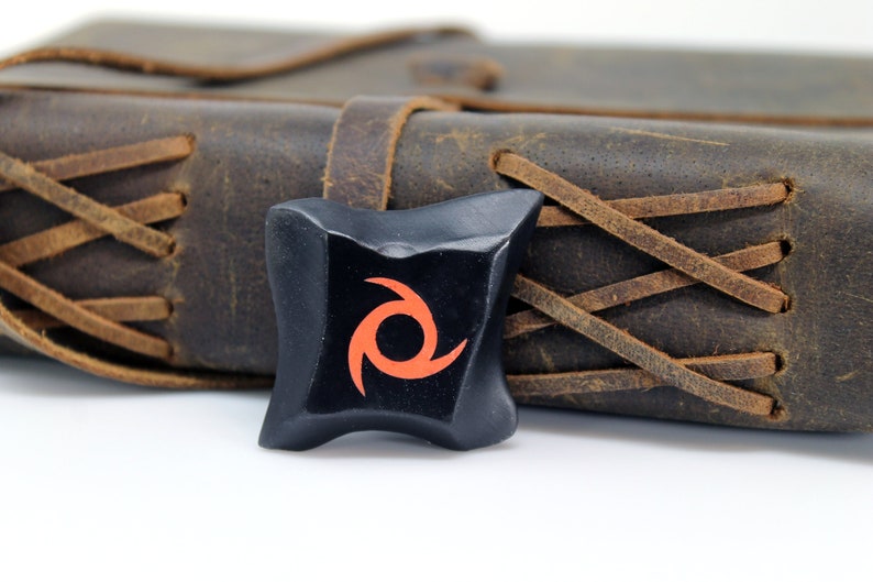 May include: A black leather-bound journal with brown leather straps and a black and orange swirl design on the front cover.