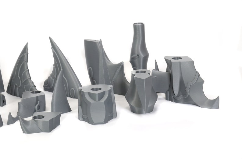 Peut inclure: Un ensemble de pi&egrave;ces en plastique gris imprim&eacute;es en 3D, probablement pour un kit de mod&eacute;lisme ou un jeu de figurines. Les pi&egrave;ces sont d&eacute;taill&eacute;es et complexes, avec des bords et des pointes ac&eacute;r&eacute;s.