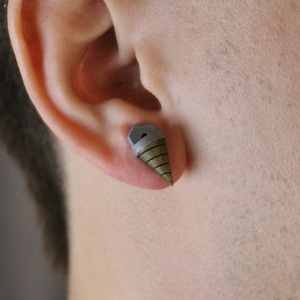 May include: A single stud earring shaped like a drill bit, with a gray top and a bronze-colored, cone-shaped drill. The earring is worn in an ear piercing.