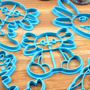 May include: A set of five blue plastic cookie cutters shaped like various animals. The cutters are on a wooden surface.