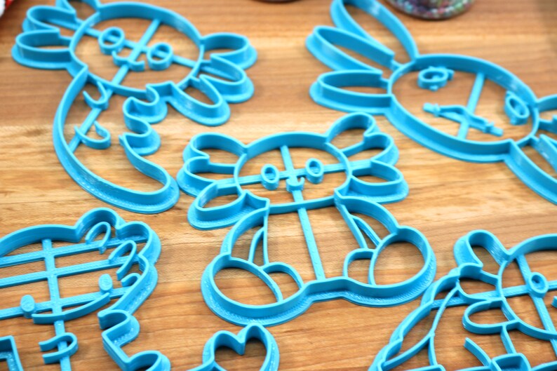 May include: A set of five blue plastic cookie cutters shaped like various animals. The cutters are on a wooden surface.
