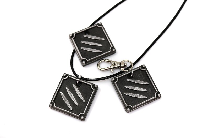 K&ouml;nnte beinhalten: Drei schwarze Metallanh&auml;nger mit einem silbernen Krallenmuster. Die Anh&auml;nger sind an einer schwarzen Schnurkette mit einem silbernen Verschluss befestigt.
