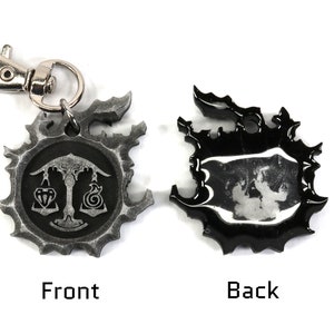 May include: A silver metal keychain with a black and white design. The front features a scale with a diamond and a spiral design. The back is black with a silver design.