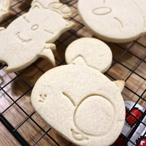 May include: Four white sugar cookies on a black wire cooling rack. The cookies are shaped like cartoon animals with simple facial features.