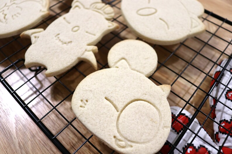 May include: Four white sugar cookies on a black wire cooling rack. The cookies are shaped like cartoon animals with simple facial features.