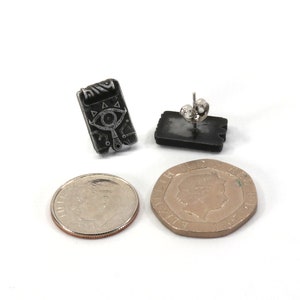 May include: A pair of black and silver earrings featuring a stylized eye design. The earrings are shown next to a US dime for size comparison.