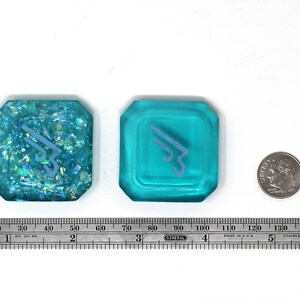 May include: Two turquoise blue resin dice with a white symbol on each. One die has a glittery finish.