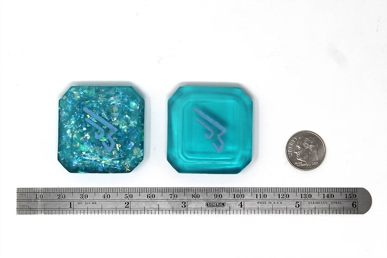 May include: Two turquoise blue resin dice with a white symbol on each. One die has a glittery finish.