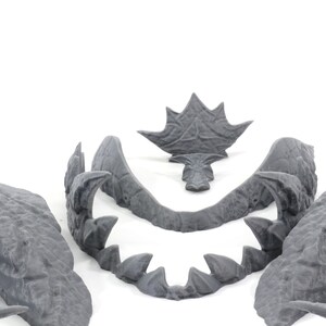 May include: A set of five gray plastic pieces that can be assembled to create a dragon head. The pieces include the top of the head, the jaw, and two side pieces.