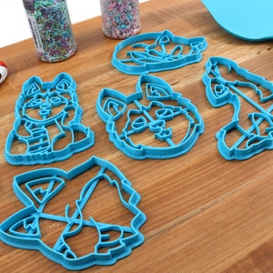 K&ouml;nnte beinhalten: Satz mit sechs blauen Plastik-Ausstechern in Form verschiedener Husky-Hundeposen. Die Ausstecher befinden sich auf einer Holzoberfl&auml;che.