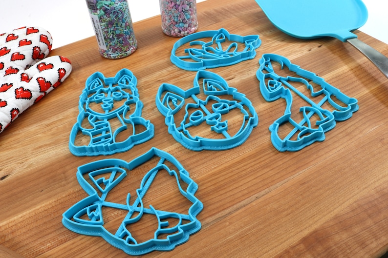 K&ouml;nnte beinhalten: Satz mit sechs blauen Plastik-Ausstechern in Form verschiedener Husky-Hundeposen. Die Ausstecher befinden sich auf einer Holzoberfl&auml;che.