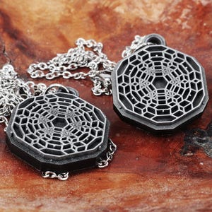 May include: Two silver necklaces with geometric pendant charms. The pendants are octagonal and feature a detailed, intricate design.