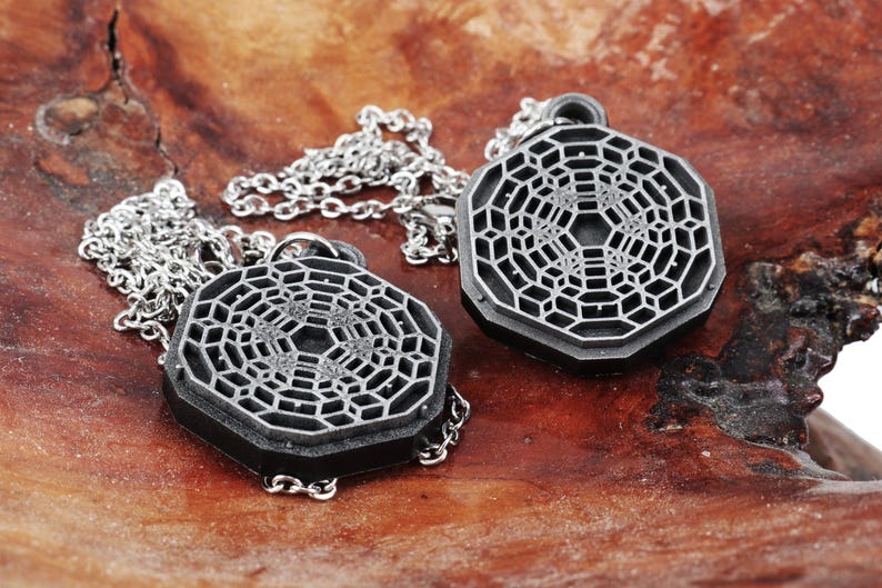 May include: Two silver necklaces with geometric pendant charms. The pendants are octagonal and feature a detailed, intricate design.