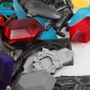 May include: A collection of colorful plastic game pieces, including red, blue, and purple gems, a silver spaceship, and a black and silver gun.