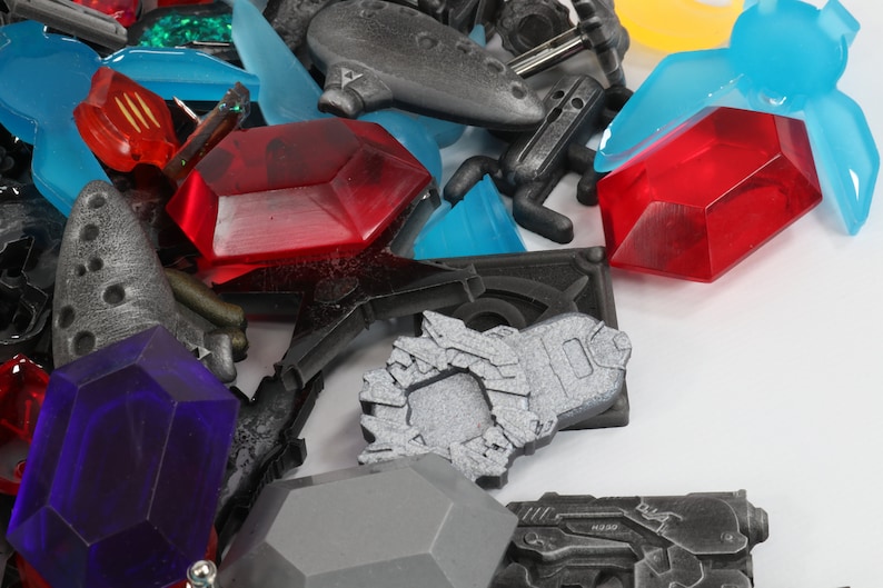 May include: A collection of colorful plastic game pieces, including red, blue, and purple gems, a silver spaceship, and a black and silver gun.