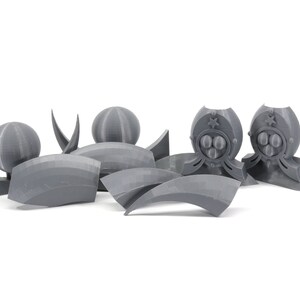 May include: A set of gray 3D printed plastic pieces for a model kit. The pieces include spheres, curved shapes, and a piece with a star and three circles.