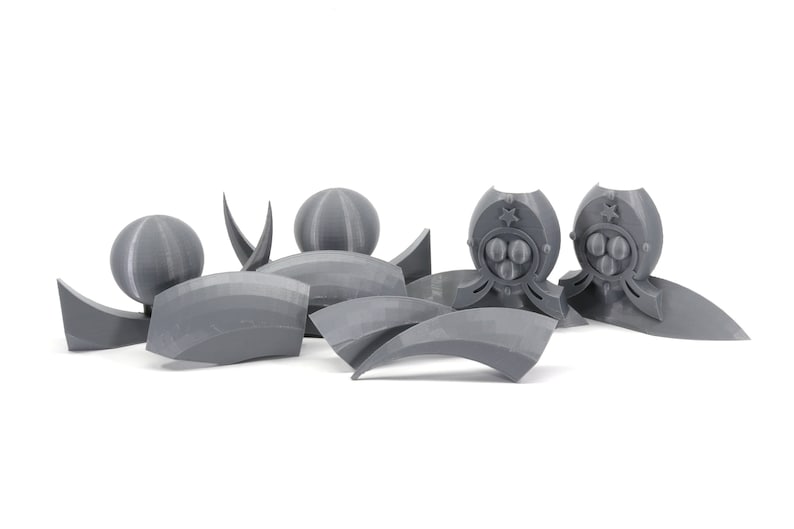 May include: A set of gray 3D printed plastic pieces for a model kit. The pieces include spheres, curved shapes, and a piece with a star and three circles.