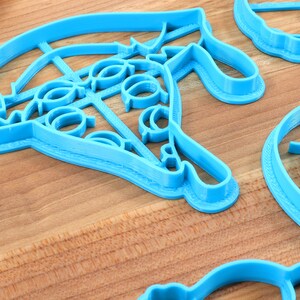 May include: A set of four blue plastic cookie cutters, each with a different design. The cutters are on a wooden surface.