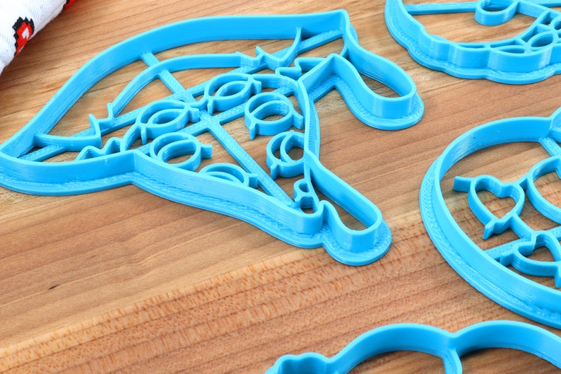 May include: A set of four blue plastic cookie cutters, each with a different design. The cutters are on a wooden surface.