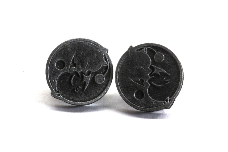 May include: A pair of black metal earrings with a circular design featuring a stylized bat and moon motif.