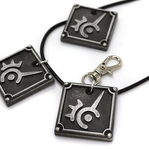 May include: Three silver-colored pendants with a black and silver symbol on each. The pendants are attached to black cords, one of which has a silver clasp.