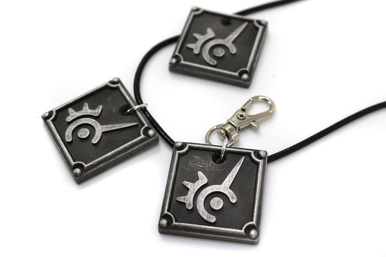 May include: Three silver-colored pendants with a black and silver symbol on each. The pendants are attached to black cords, one of which has a silver clasp.