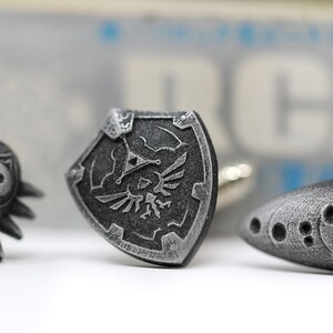 May include: Three silver cufflinks featuring iconic symbols from the Legend of Zelda video game series: the Triforce, the Master Sword, and the Ocarina of Time.