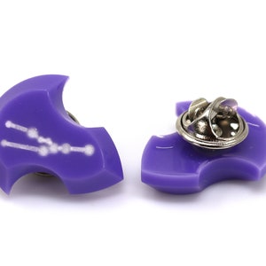 Op de afbeelding: Paarse emaille pin met een wit sterrenbeeld ontwerp. De pin heeft een metalen sluiting aan de achterkant.