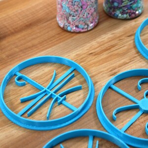 Op de afbeelding: Vier blauwe plastic koekjesvormen op een houten oppervlak. De vormen zijn in verschillende ontwerpen, waaronder een basketbal, een letter en een werveling.