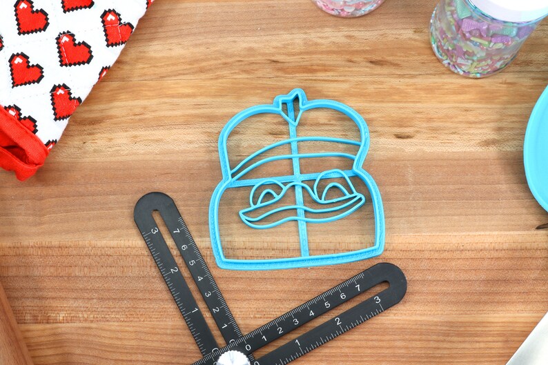 Puede incluir: Un cortador de galletas de pl&aacute;stico azul con forma de personaje de dibujos animados con una corona en la cabeza. El personaje tiene una amplia sonrisa y ojos grandes.