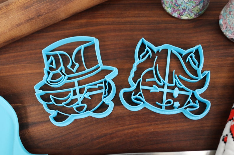 May include: Two blue plastic cookie cutters, one shaped like a person wearing a hat and the other shaped like a person with a ponytail.