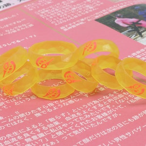May include: A group of eight yellow silicone rings with a red design. The rings are stacked on top of each other.