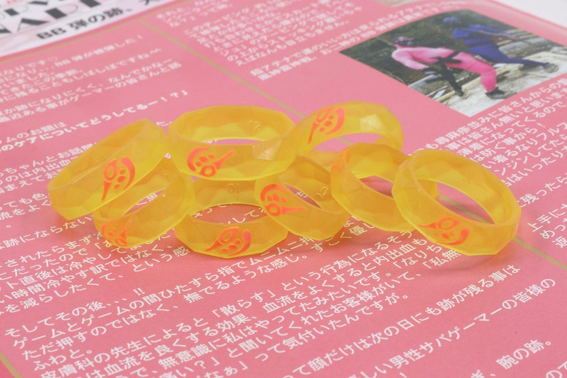 May include: A group of eight yellow silicone rings with a red design. The rings are stacked on top of each other.