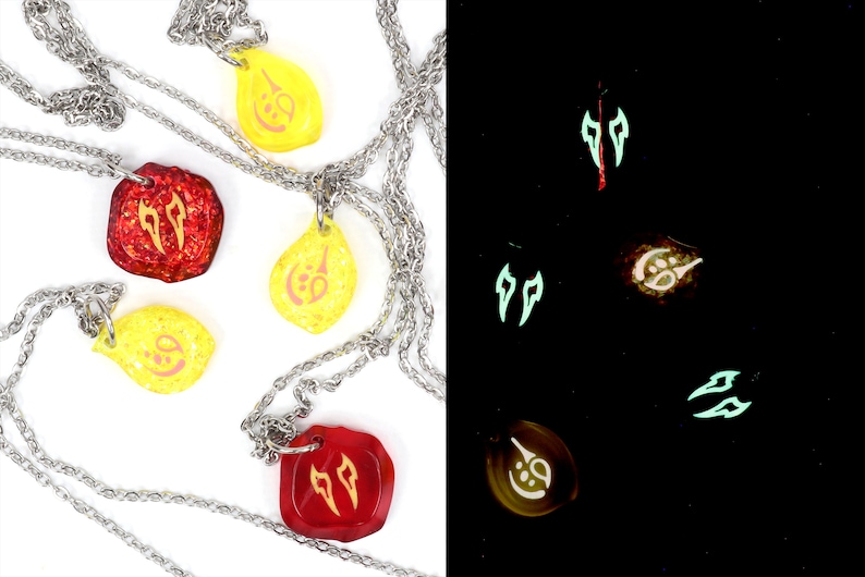 May include: Four necklaces with glow-in-the-dark pendants. The pendants are red, yellow, and a combination of red and yellow. The pendants feature different symbols. The necklaces are on a white background. The right side of the image shows the pendants glowing in the dark.