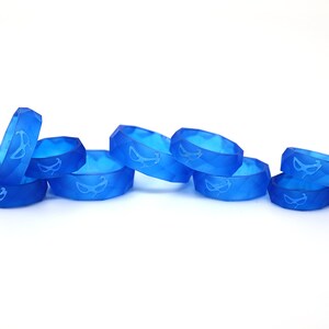 May include: A group of eight blue silicone rings with a white mask design. The rings are stacked and arranged in a row on a white surface.