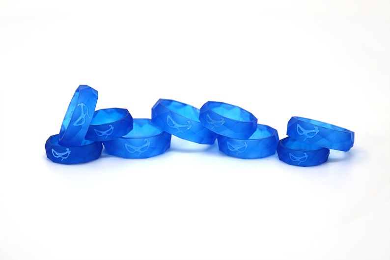 May include: A group of eight blue silicone rings with a white mask design. The rings are stacked and arranged in a row on a white surface.
