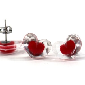 Puede incluir: Un par de pendientes transparentes en forma de coraz&oacute;n con corazones rojos en su interior. Los pendientes tienen postes de plata.