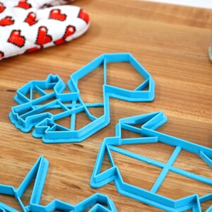 May include: Four blue plastic cookie cutters shaped like origami figures. The cutters are on a wooden surface.