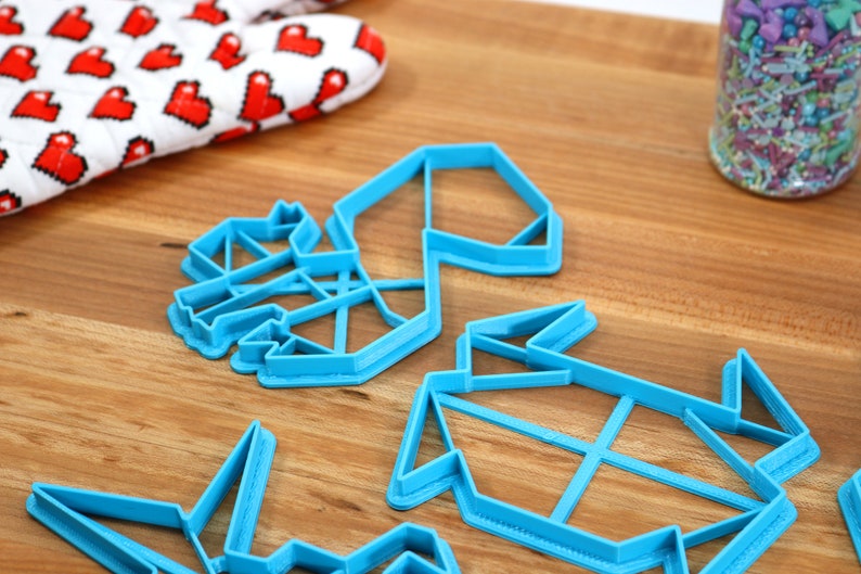 May include: Four blue plastic cookie cutters shaped like origami figures. The cutters are on a wooden surface.