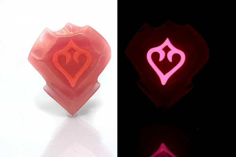 May include: A pink resin heart-shaped charm with a glowing pink heart design. The charm glows in the dark.