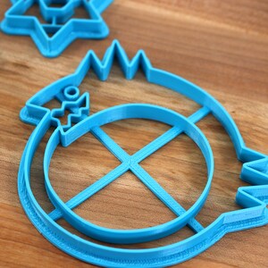 May include: A set of three blue plastic cookie cutters. The cutters are shaped like a star, a circle with a cross inside, and a fish with a circle inside.