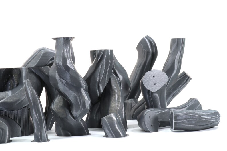Puede incluir: Una colecci&oacute;n de 10 esculturas abstractas grises impresas en 3D con un acabado texturizado similar a la madera. Las esculturas est&aacute;n dispuestas en un grupo sobre un fondo blanco.