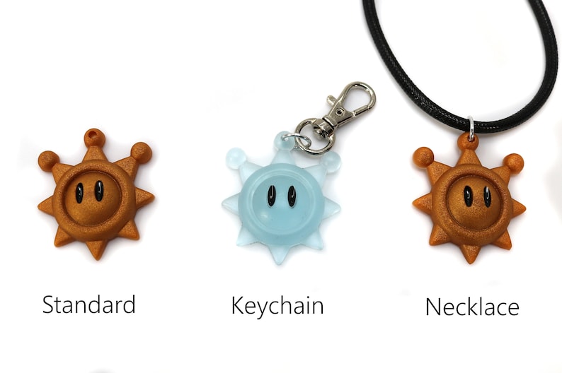 May include: Three versions of a gold-colored sun-shaped pendant with black eyes. The pendant is available as a standard charm, a keychain, and a necklace.