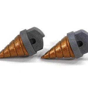 May include: Two metallic drill bits with a bronze-colored, spiral-shaped tip and a gray, hexagonal base. The drill bits are designed for use with power tools and are set against a white background.