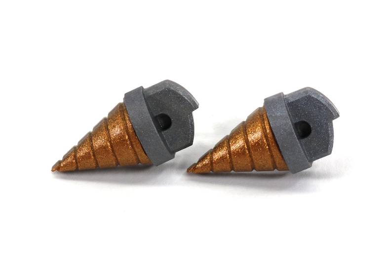 May include: Two metallic drill bits with a bronze-colored, spiral-shaped tip and a gray, hexagonal base. The drill bits are designed for use with power tools and are set against a white background.